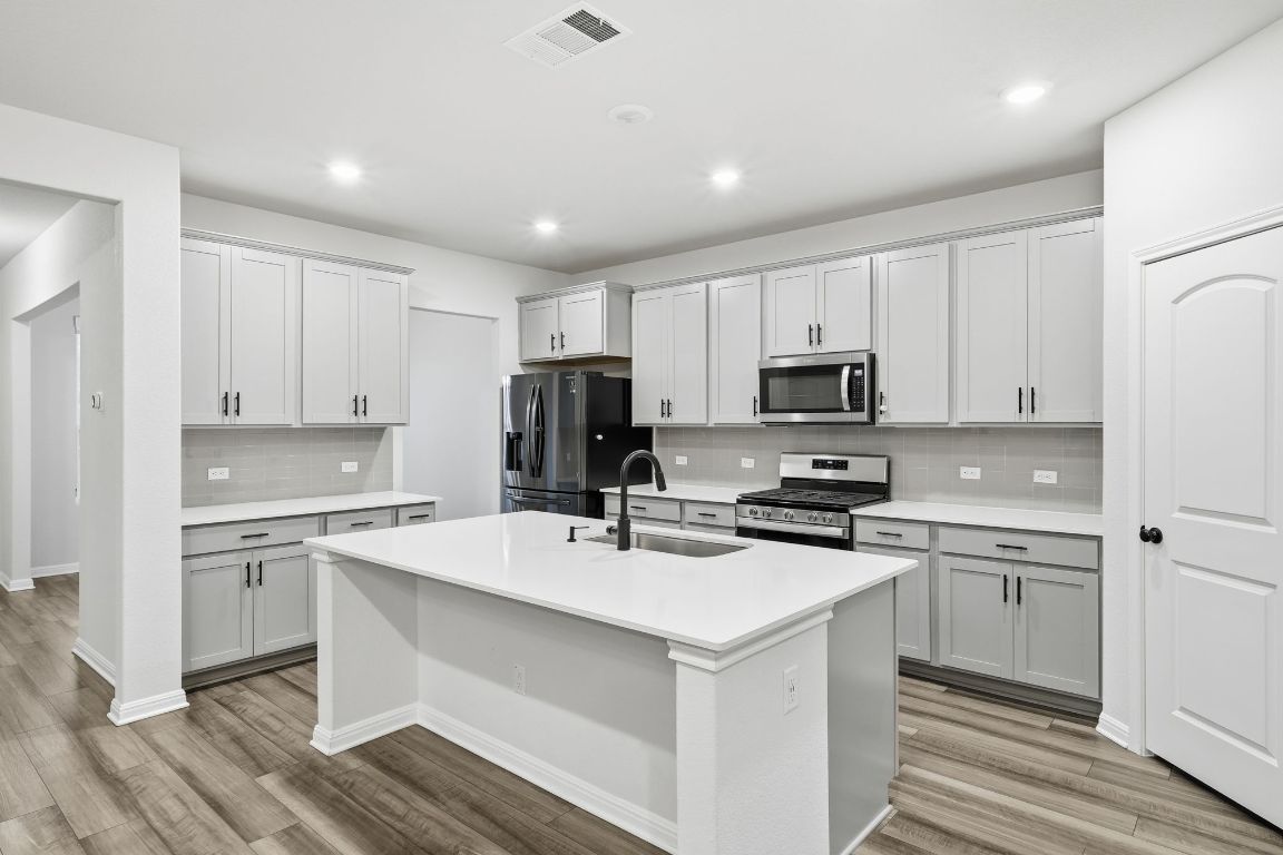 1941 Winston Way Leander, TX 78641 - Photo 5 of 28 Kitchen featuring appliances with stainless steel finishes, an island with sink, light wood-style floors, recessed lighting, and backsplash