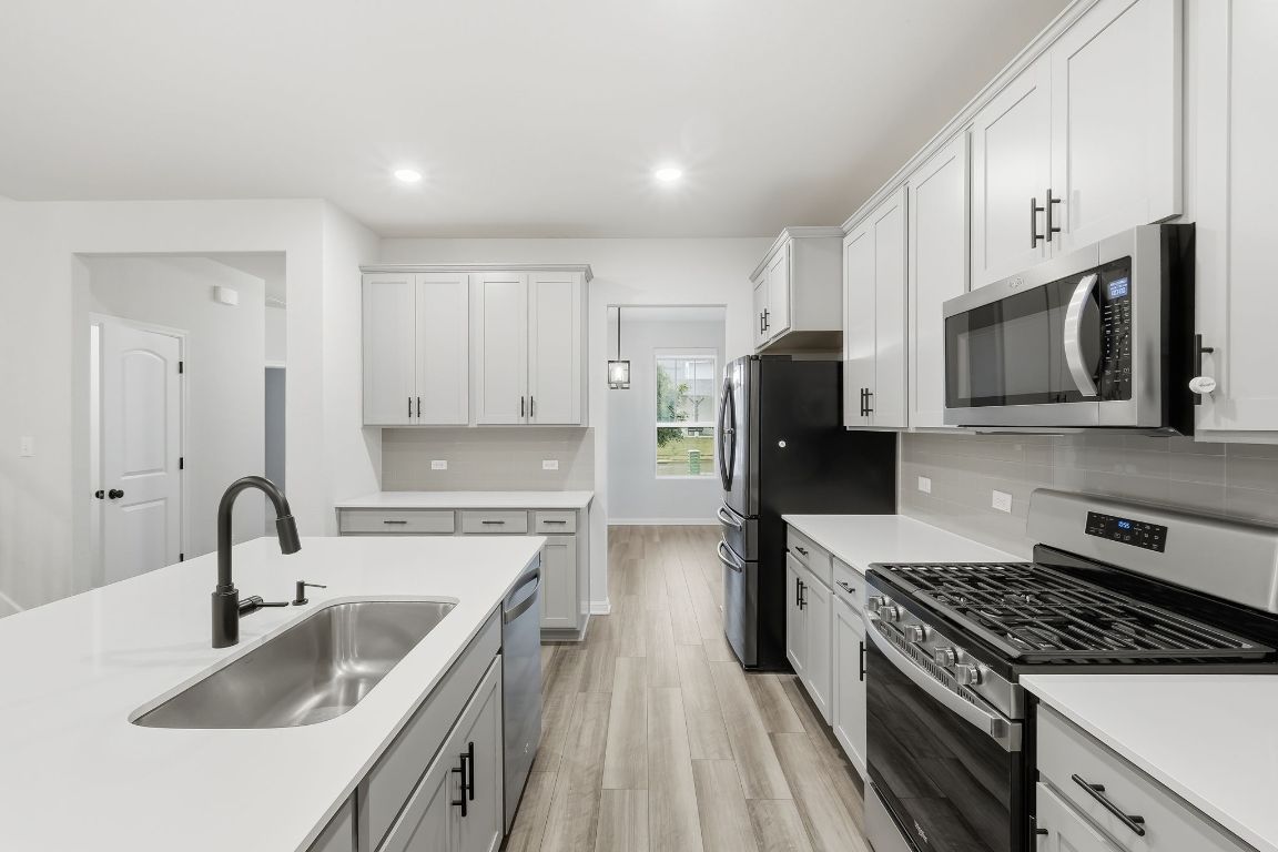 1941 Winston Way Leander, TX 78641 - Photo 6 of 28 Kitchen featuring appliances with stainless steel finishes, decorative backsplash, light wood finished floors, white cabinetry, and recessed lighting