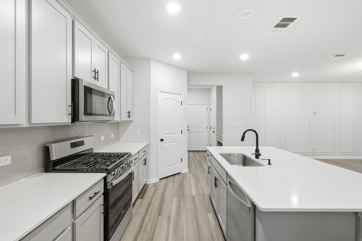 1941 Winston Way Leander, TX 78641 - Photo 8 of 28 Kitchen with appliances with stainless steel finishes, a center island with sink, gray cabinetry, tasteful backsplash, and light wood-style flooring