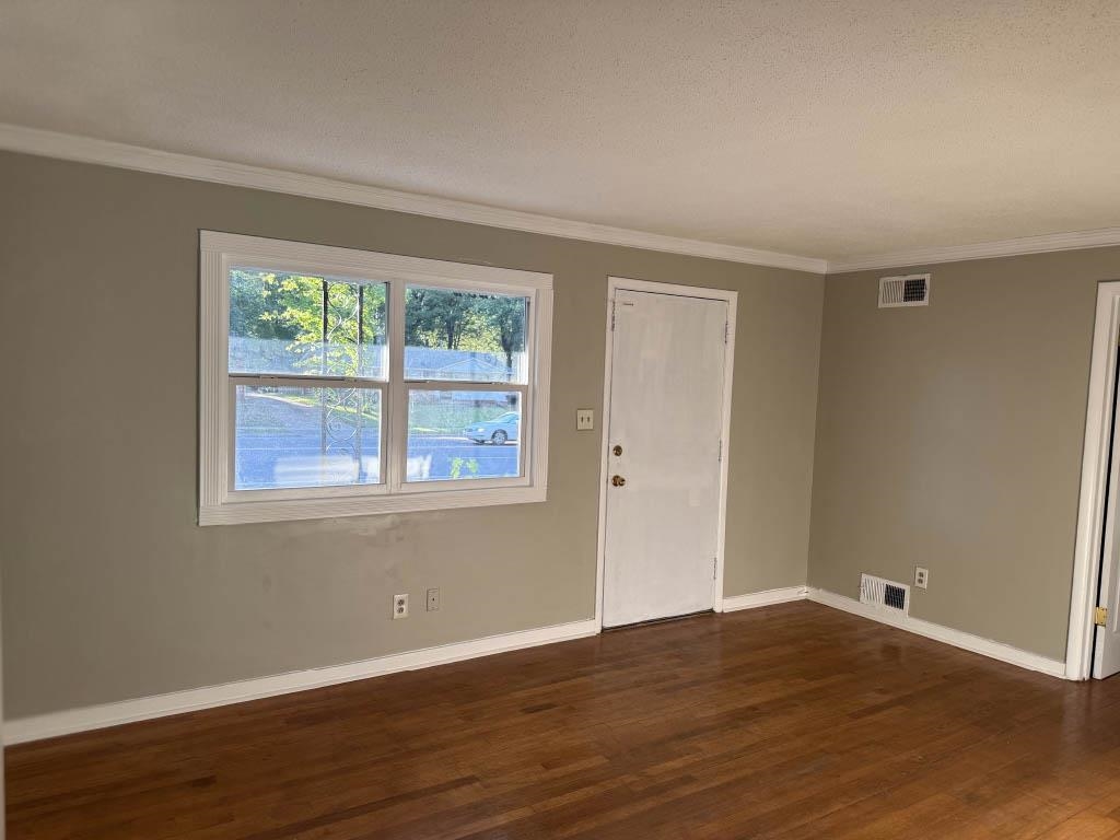 Empty room with crown molding and dark wood-style flooring