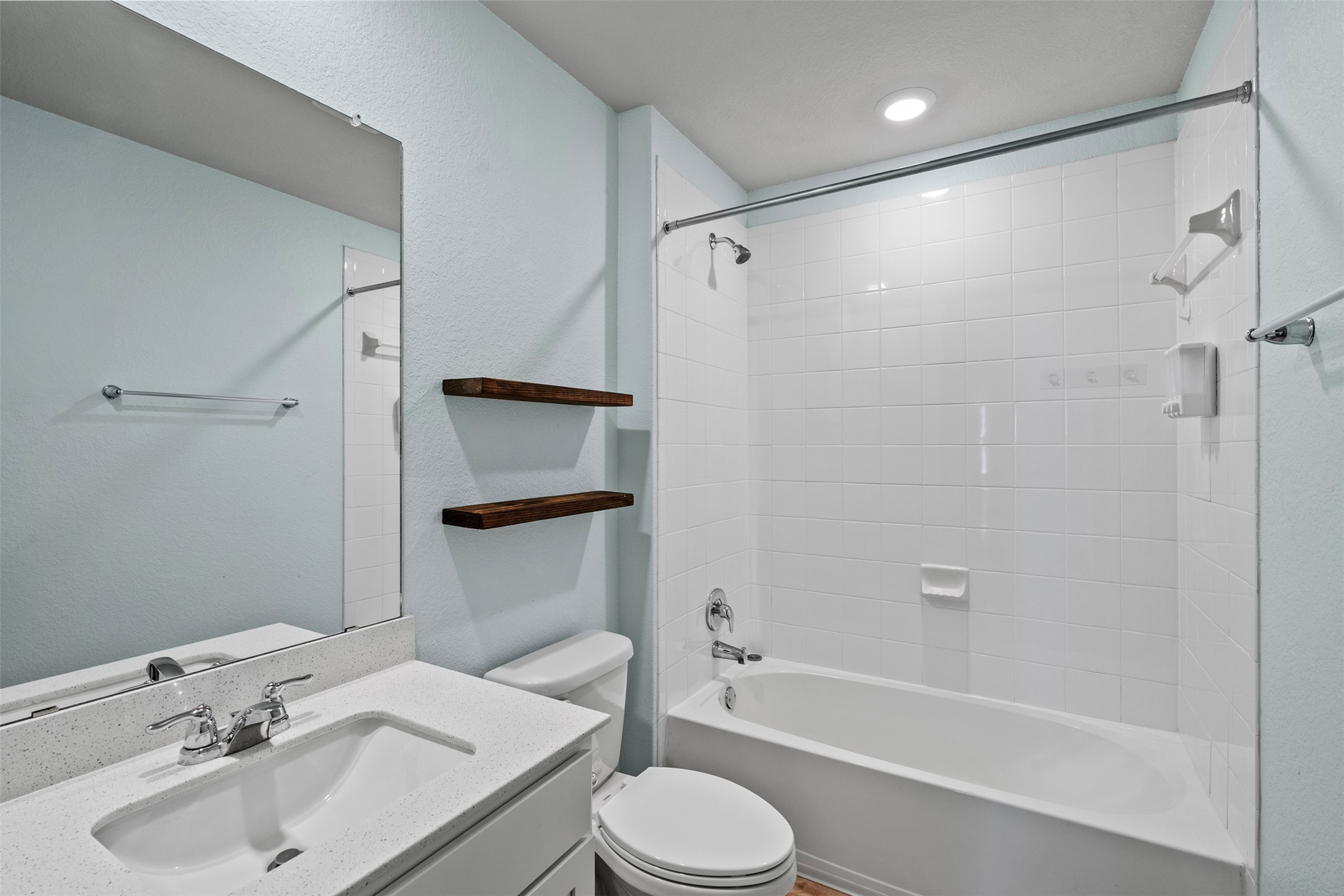120 Ellinger Road Georgetown, TX 78626 - Photo 25 of 28 Bathroom with light blue walls, a white vanity featuring a rectangular sink and a speckled countertop, a large mirror, and two dark wood floating shelves