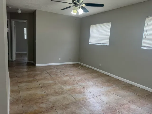 an empty room with chandelier fan and windows