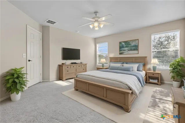 a spacious bedroom with a large bed a flat tv screen and a potted plant