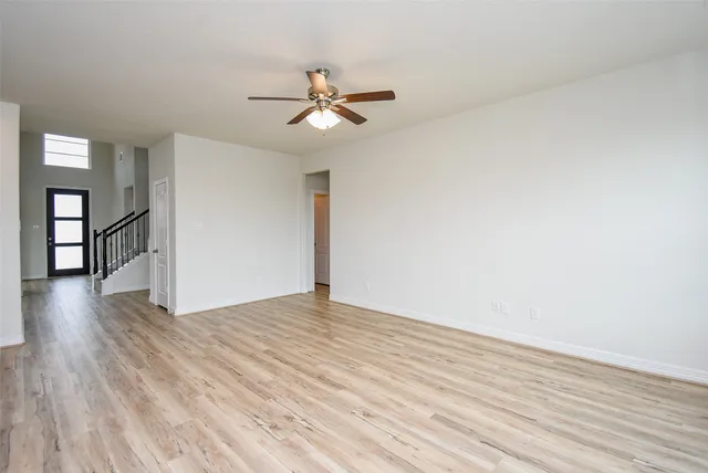 an empty room with wooden floor fan and windows