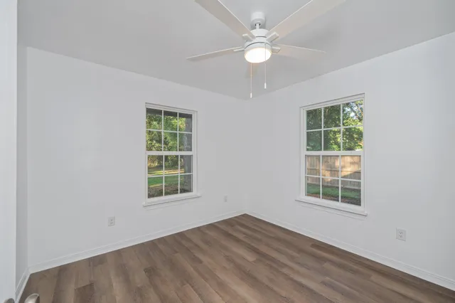 an empty room with wooden floor ceiling fan and window
