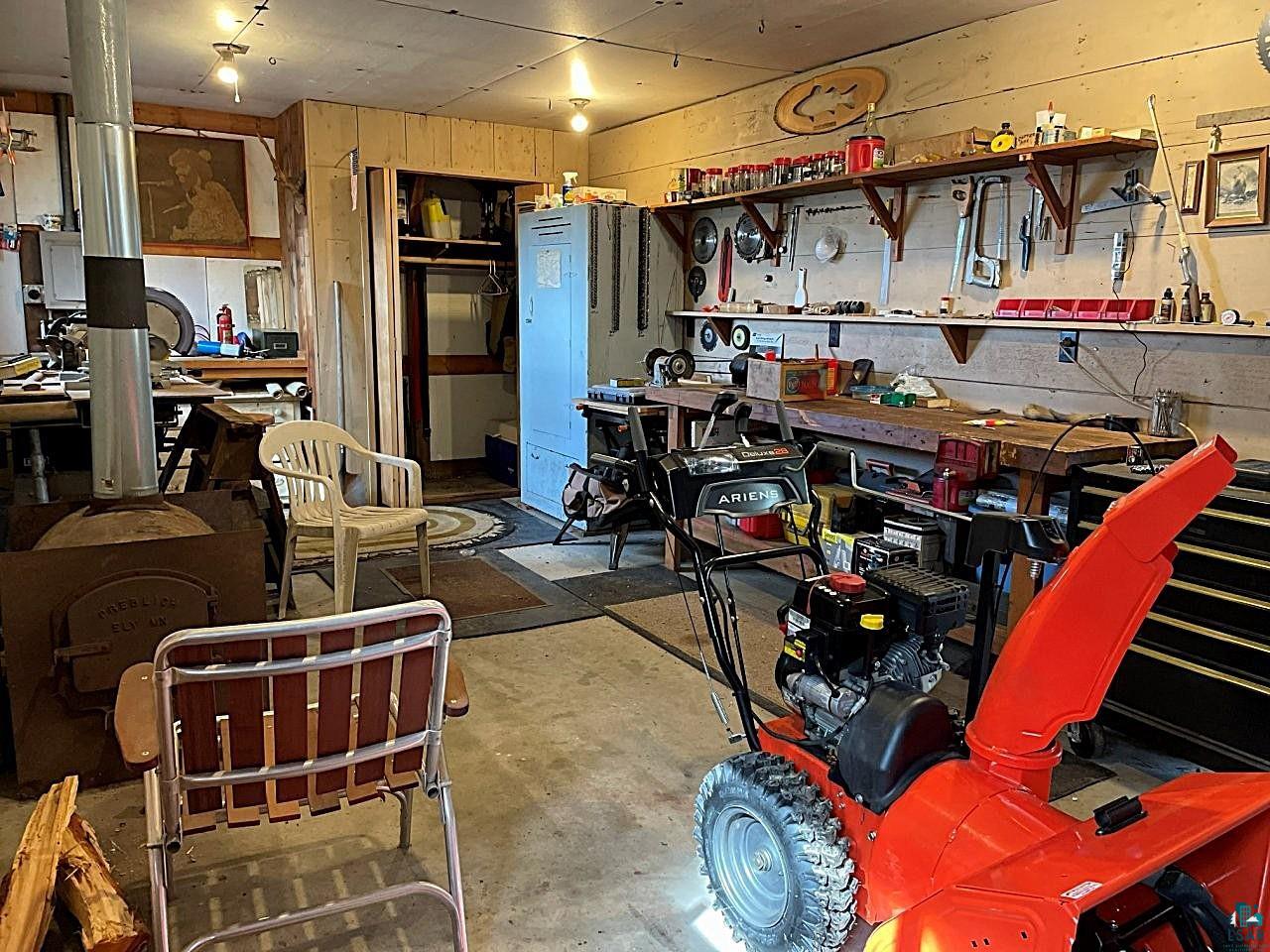 1480 Maijala Road Ely, MN 55731 - Photo 40 of 58 Versatile workspace featuring concrete flooring, a built-in workbench with shelving, and a metal wood-burning stove with a flue