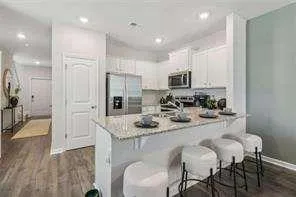 a kitchen with stainless steel appliances granite countertop a sink a stove a refrigerator and a dining table with wooden floor