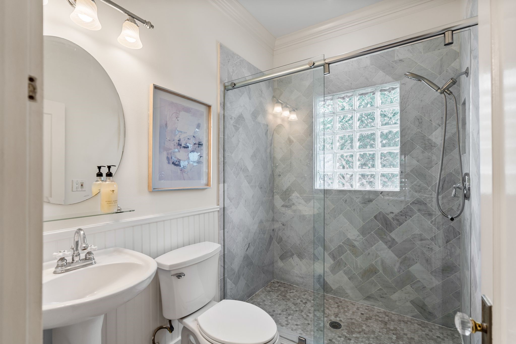 307 East 8th Street Houston, TX 77007 - Photo 22 of 35 Charming full bathroom with a glass-enclosed walk-in shower featuring a herringbone tile surround and pebble-style shower floor. Additional details include a pedestal sink, round wall mirror, and classic beadboard wall accents for timeless character.