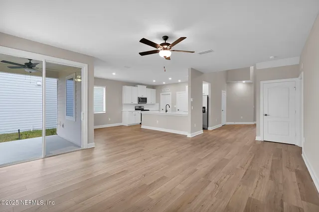 a view of an empty room and kitchen with wooden floor