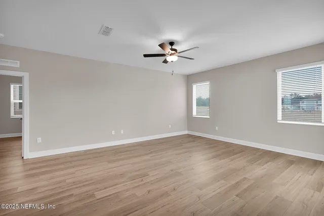 an empty room with wooden floor ceiling fan and windows