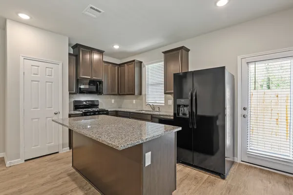 a kitchen with granite countertop a refrigerator a sink a stove a microwave and wooden floor