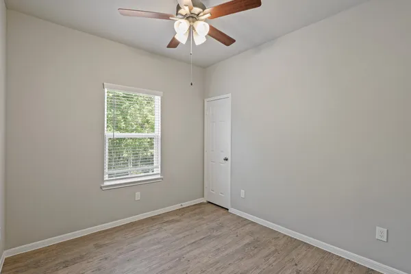 an empty room with wooden floor fan and windows