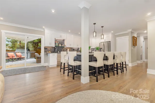 a large white dining hall with stainless steel appliances kitchen island granite countertop a dining table chairs and a large window