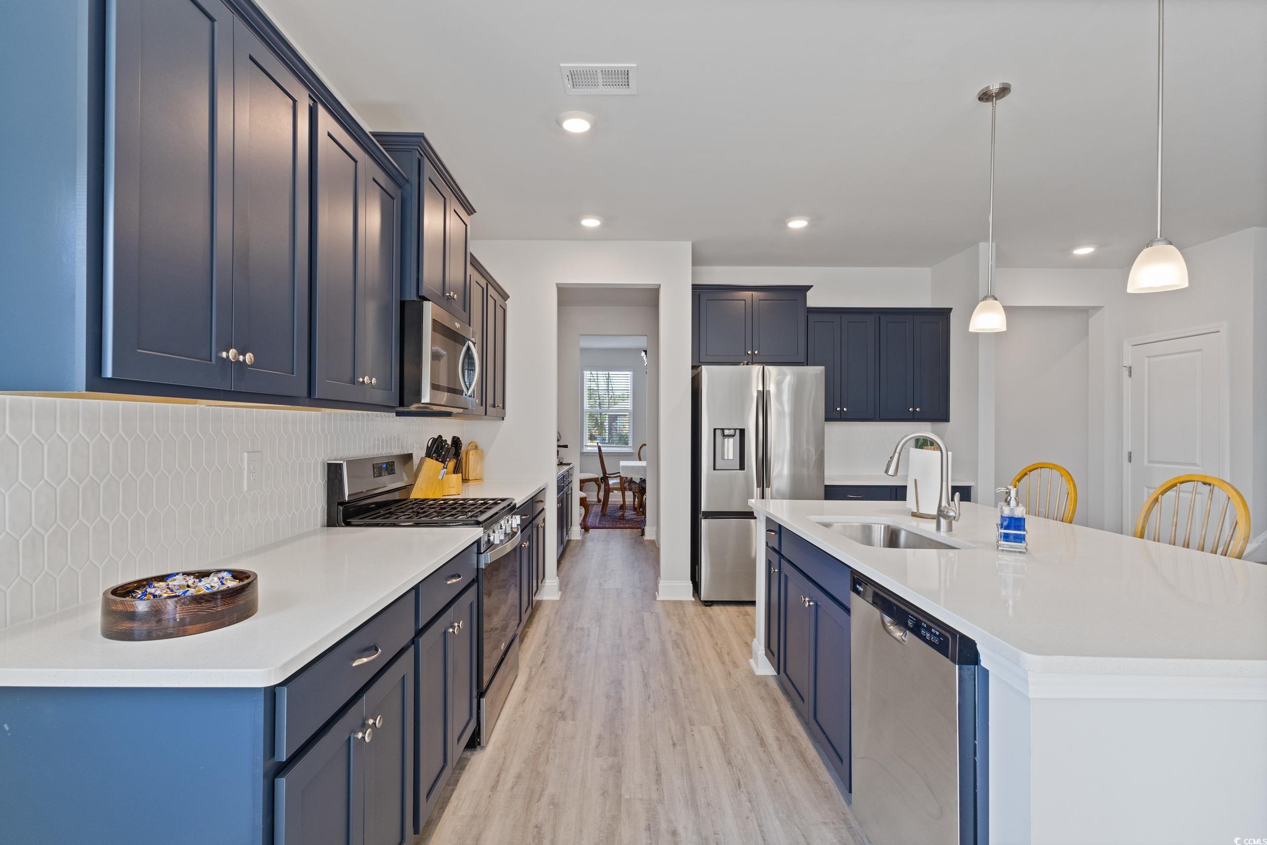 4070 Rutherford Court Little River, SC 29566 - Photo 10 of 40 Kitchen with stainless steel appliances, hanging light fixtures, blue cabinets, light stone countertops, and tasteful backsplash