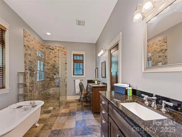 a spacious bathroom with a granite countertop double vanity sink a mirror a bathtub and shower