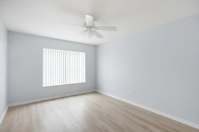 an empty room with wooden floor fan and windows
