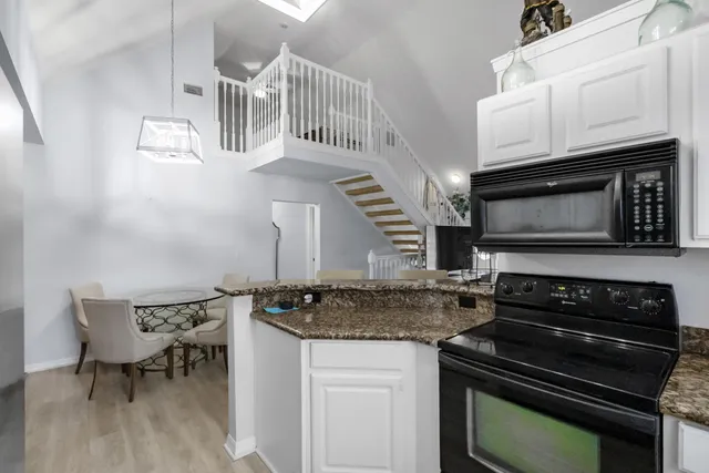 a kitchen with granite countertop a stove a microwave a sink and white cabinets