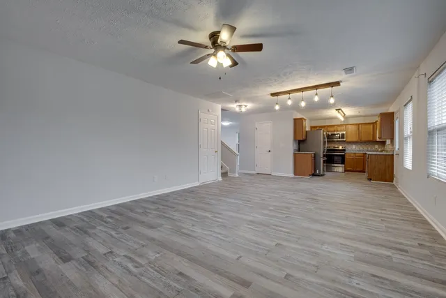 a view of an empty room with wooden floor and a ceiling fan