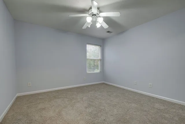an empty room with a chandelier fan and windows