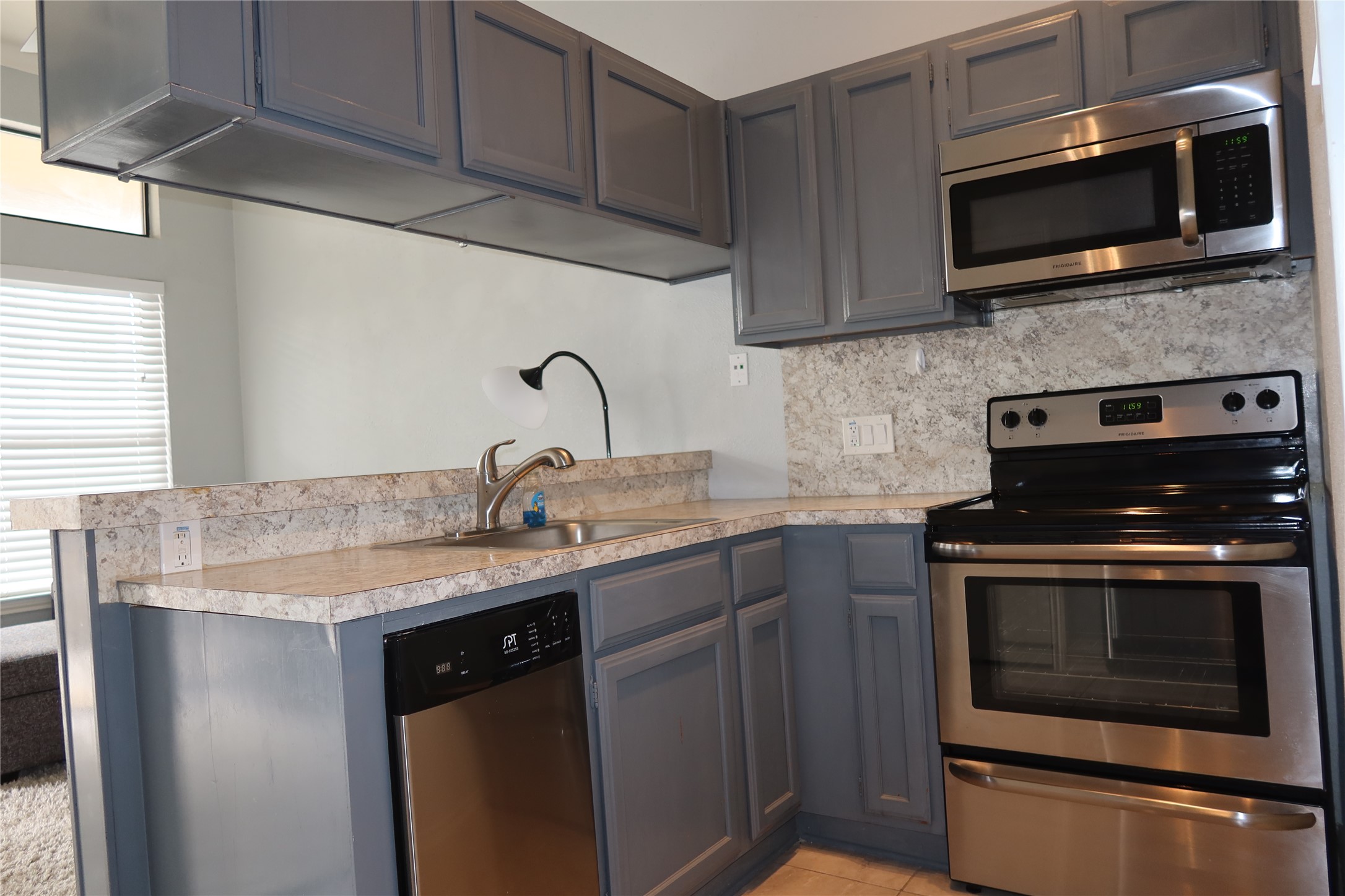 2802 Nueces Street, Unit 306 Austin, TX 78705 - Photo 7 of 20 Kitchen featuring gray cabinetry, light-toned countertops with a subtle pattern, a stainless steel sink with a gooseneck faucet, a stainless steel dishwasher, and a stainless steel range with an over-the-range microwave
