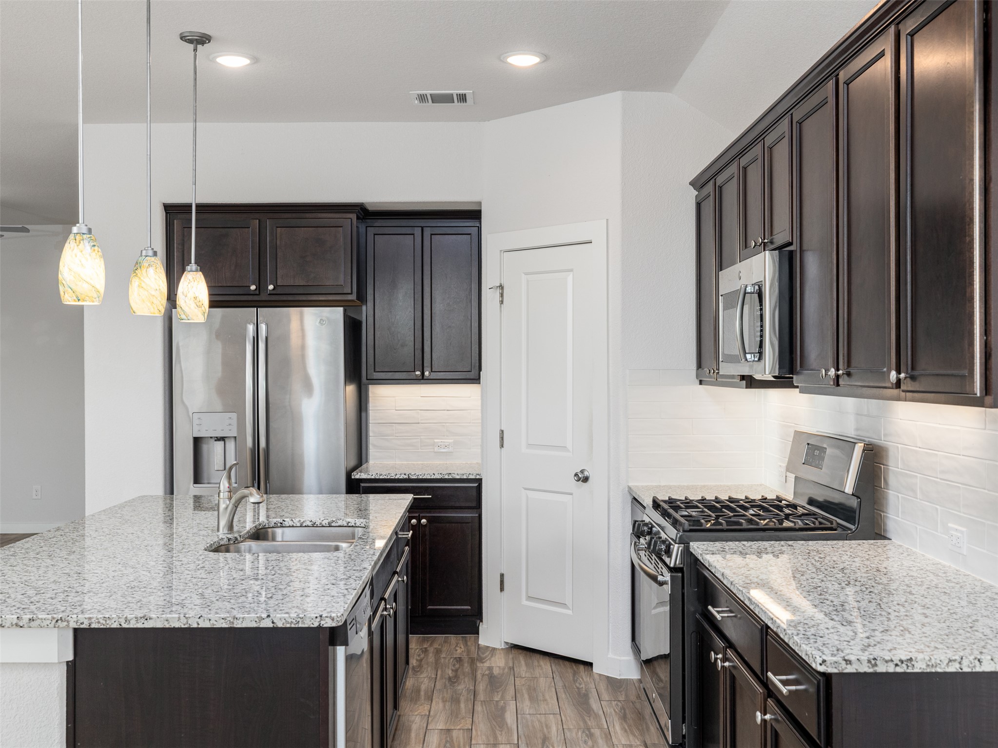 6856 Catania Loop Round Rock, TX 78665 - Photo 11 of 30 Kitchen with stainless steel appliances, hanging light fixtures, an island with sink, light wood-type flooring, and light stone counters