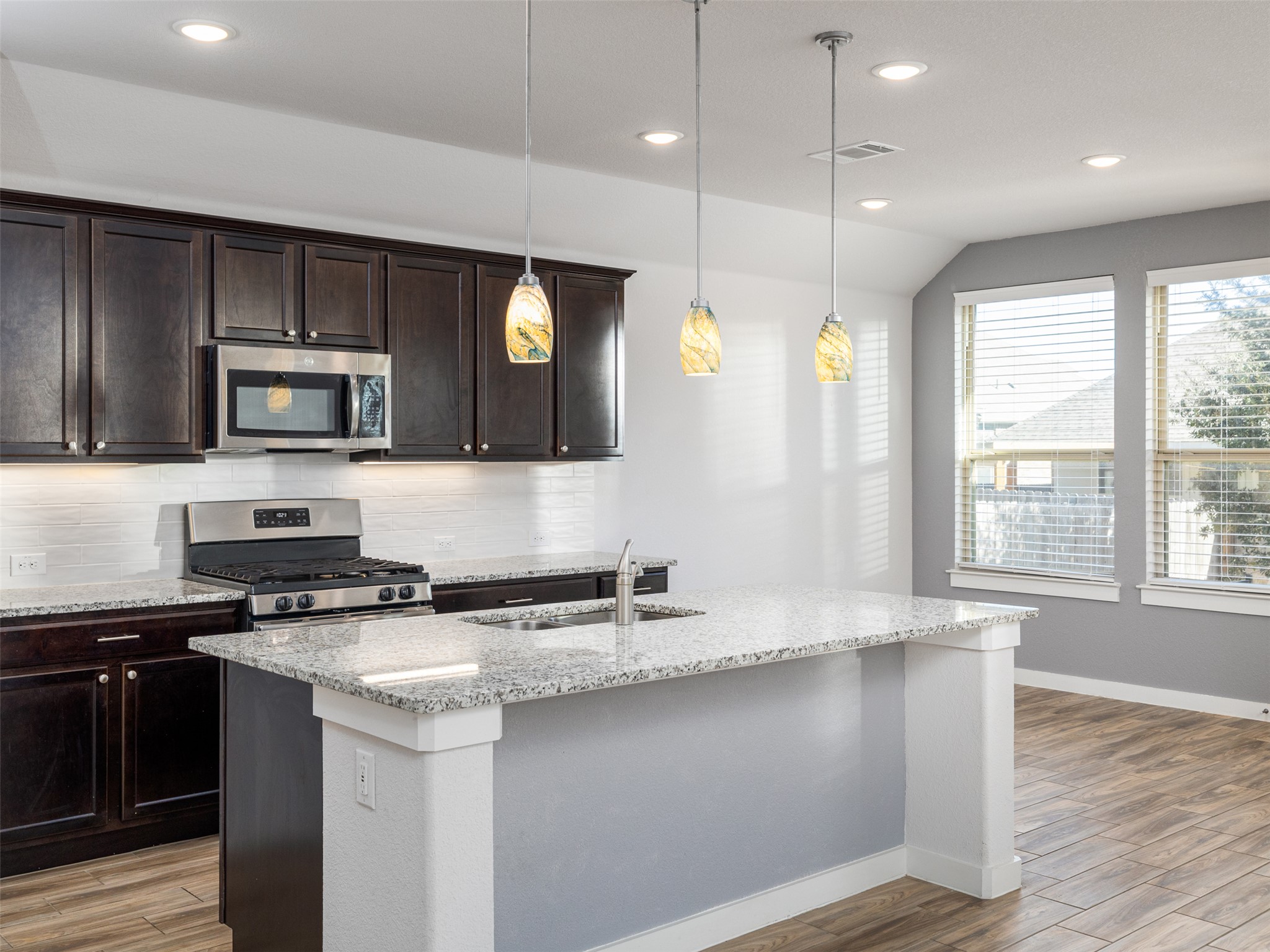 6856 Catania Loop Round Rock, TX 78665 - Photo 13 of 30 Kitchen with light wood-type flooring, stainless steel appliances, dark wood finish cabinetry, light stone countertops, and vaulted ceiling