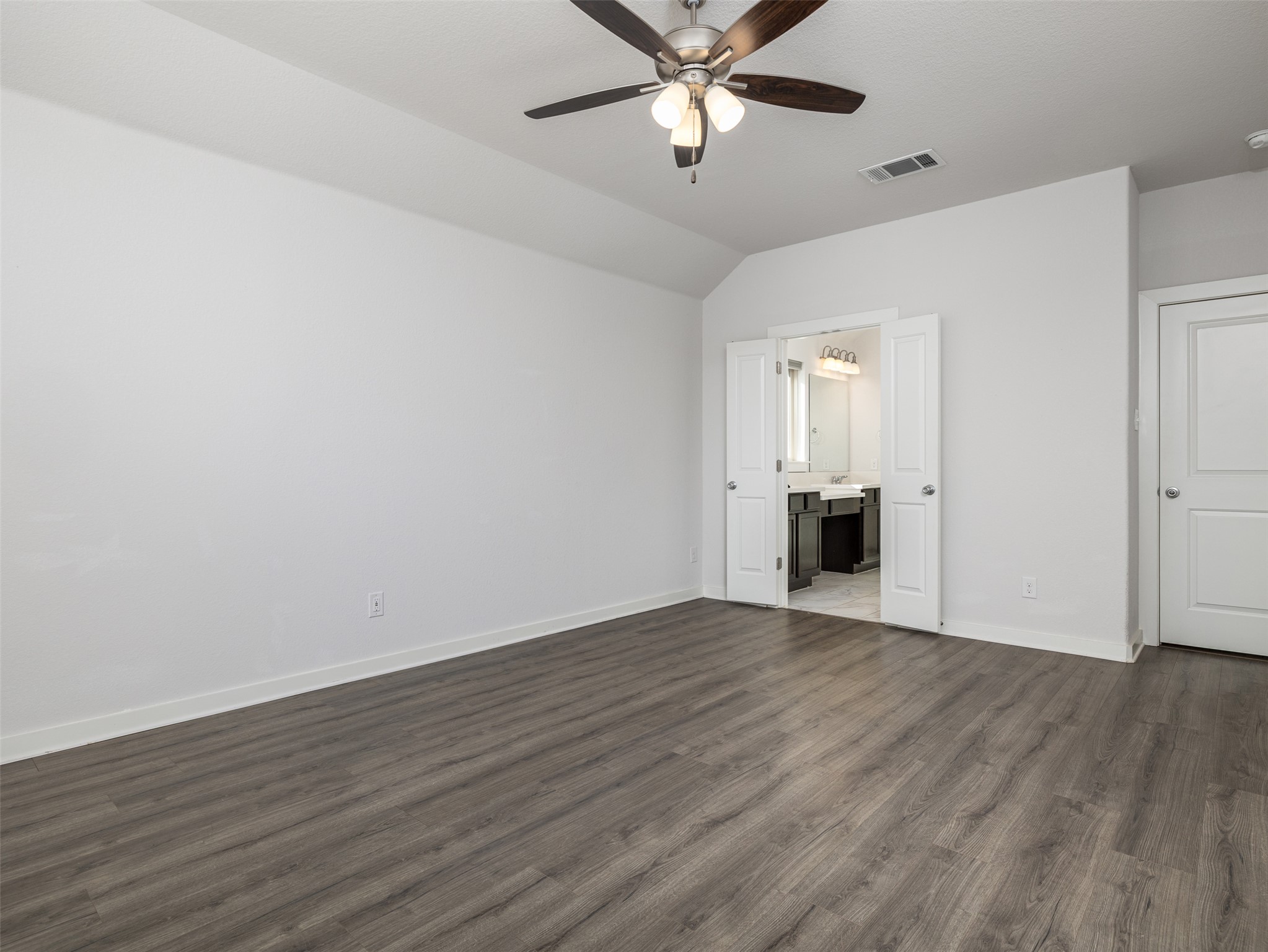 6856 Catania Loop Round Rock, TX 78665 - Photo 15 of 30 Unfurnished bedroom featuring dark wood-style flooring, a ceiling fan, vaulted ceiling, and connected bathroom