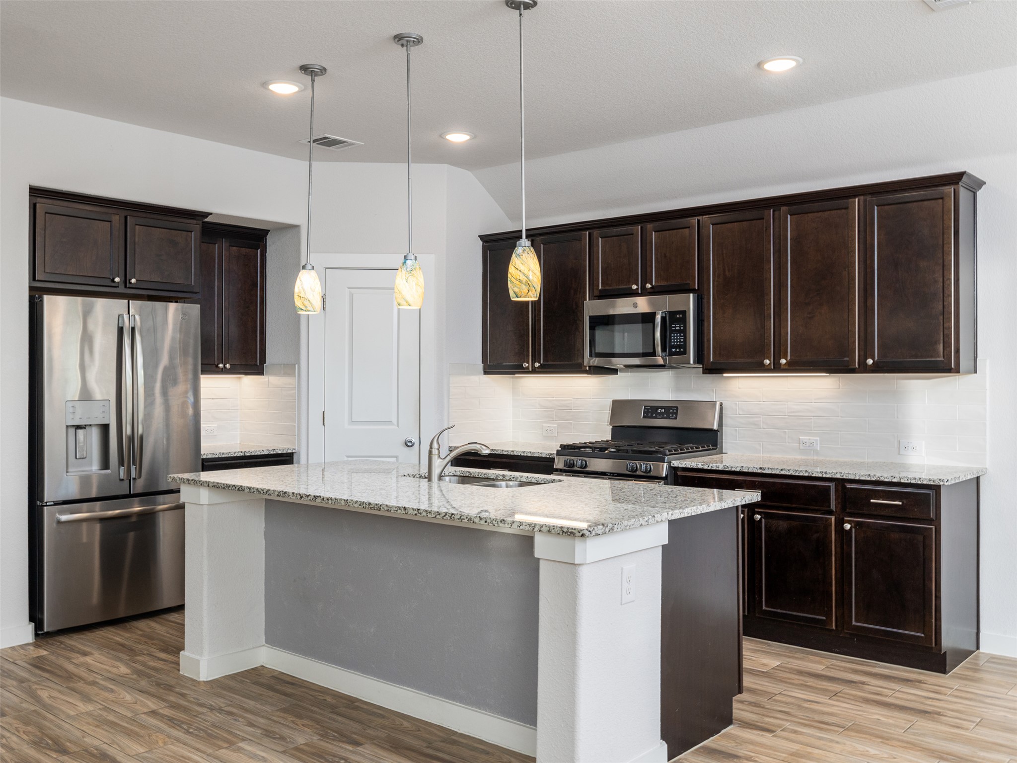 6856 Catania Loop Round Rock, TX 78665 - Photo 5 of 30 Kitchen featuring dark wood finish cabinetry, stainless steel appliances, light stone countertops, light wood finished floors, and decorative light fixtures