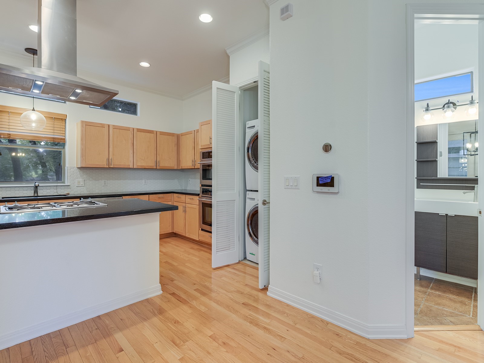1115 Kinney Avenue, Unit 9 Austin, TX 78704 - Photo 10 of 19 Kitchen with light brown cabinets, island range hood, stacked washer / drying machine, light wood finished floors, and dark countertops