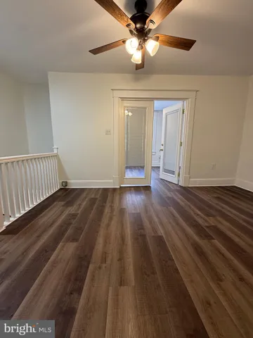 a view of an empty room with wooden floor and a ceiling fan