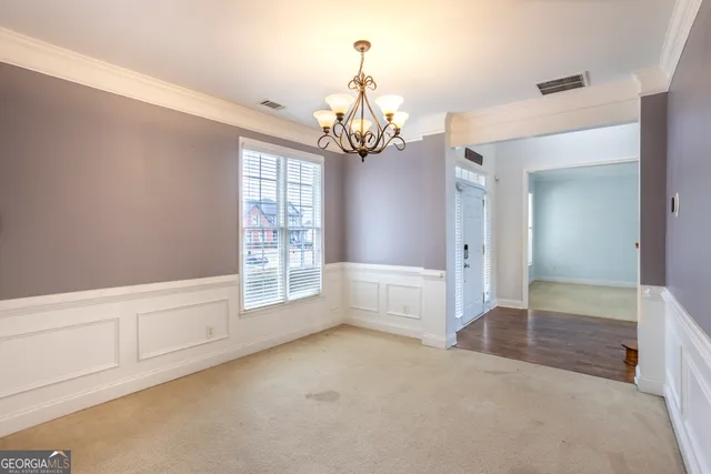 a view of an empty room with chandelier and kitchen view