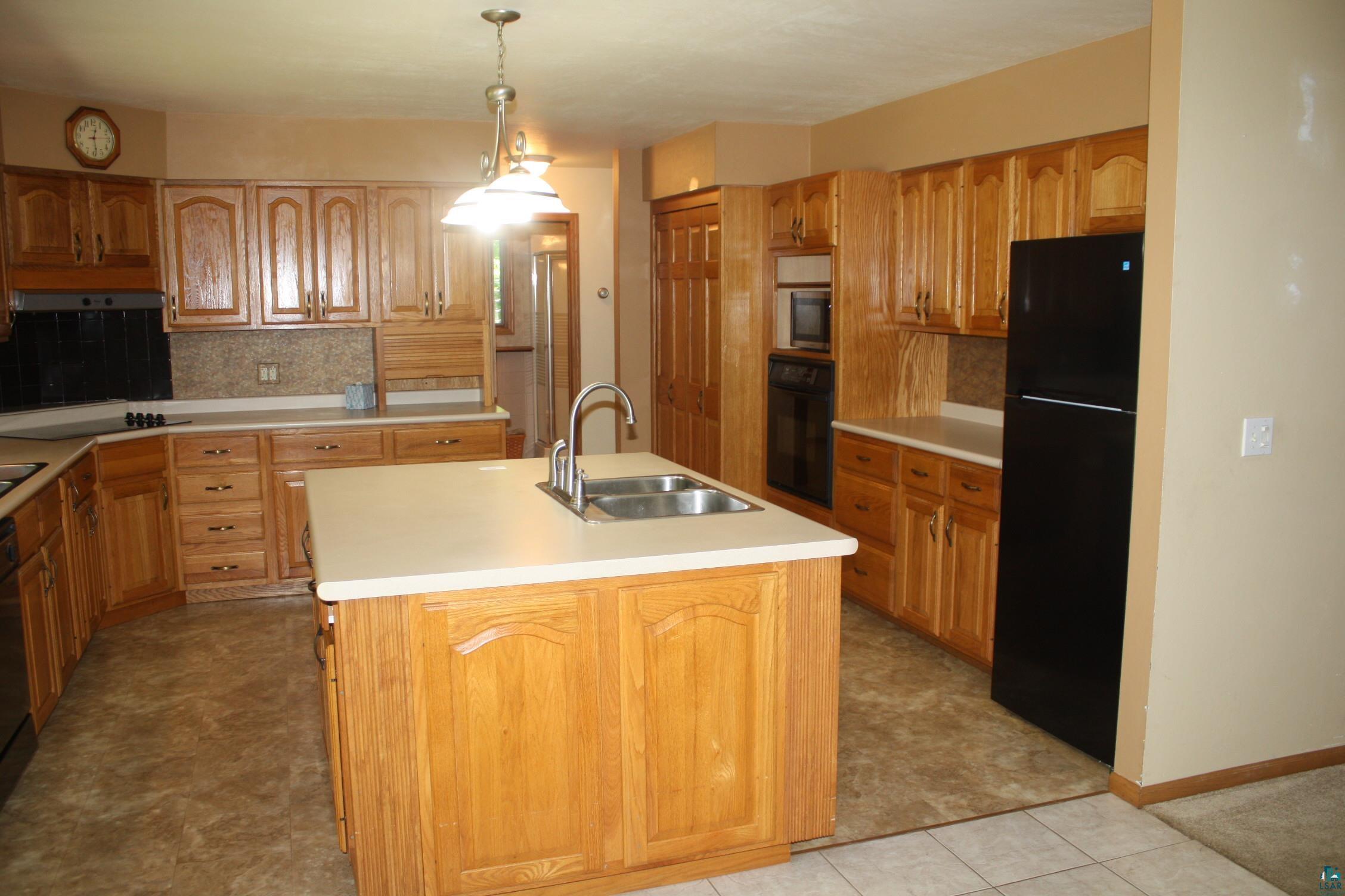 6718 East County Rd B South Range, WI 54874 - Photo 18 of 50 Kitchen featuring an island with sink, black refrigerator, sink, tasteful backsplash, and light tile floors