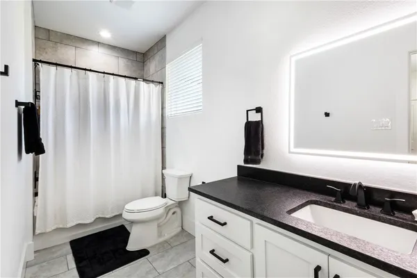 a bathroom with a granite countertop sink a toilet a mirror and shower