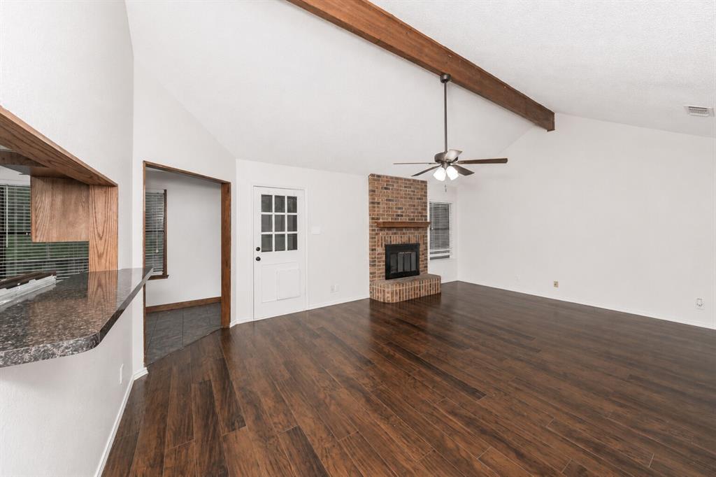 1001 Rosebud Drive Azle, TX 76020 - Photo 12 of 36 Spacious room featuring rich wood-finish flooring, a vaulted ceiling with exposed wood beams, and a brick fireplace