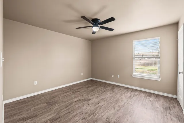 an empty room with wooden floor a ceiling fan and windows