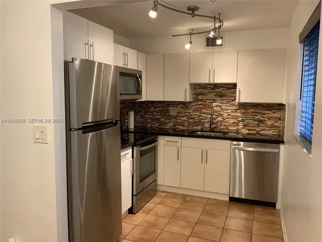 a kitchen with stainless steel appliances granite countertop a refrigerator a sink and white cabinets