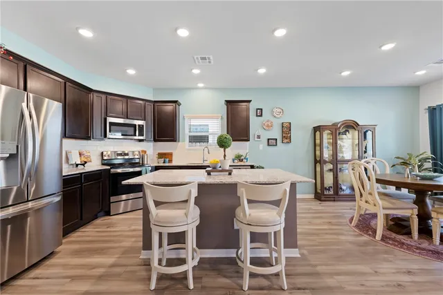 a kitchen with stainless steel appliances kitchen island granite countertop a refrigerator a stove a microwave oven with a dining table and chairs