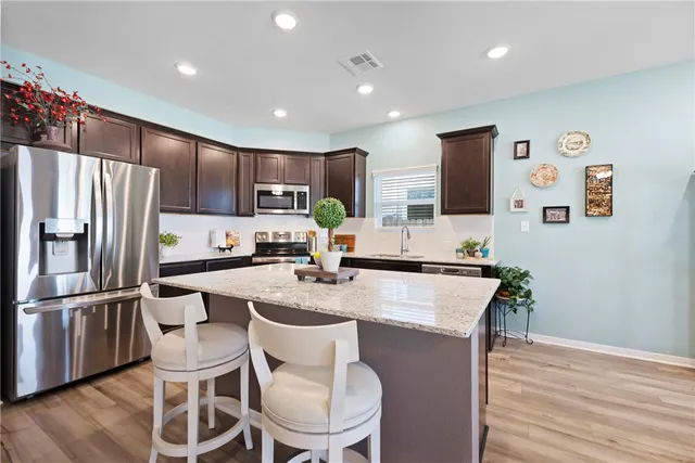 a kitchen with stainless steel appliances granite countertop a refrigerator a stove top oven a sink dishwasher and white cabinets with wooden floor