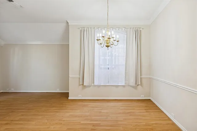 a view of an empty room with wooden floor and chandelier