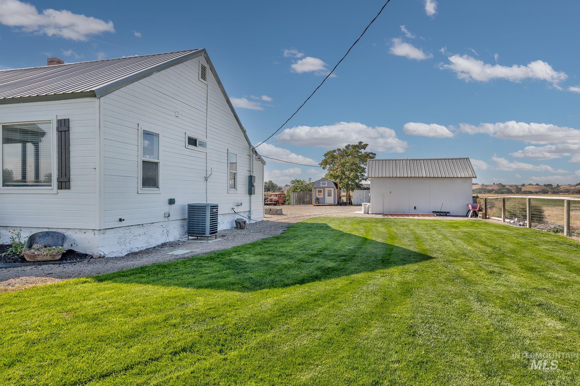 4631 Rolland Road Ontario, OR 97914 - Photo 22 of 43 White siding exterior with a metal roof, featuring an expansive green lawn, a detached shed, and a fenced perimeter
