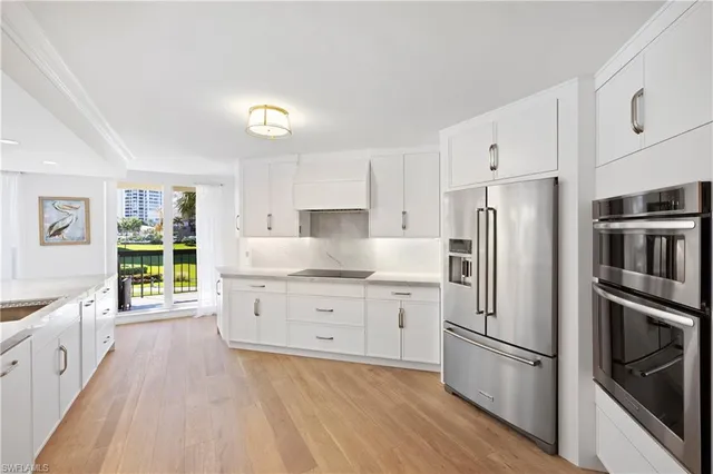 a kitchen with granite countertop a refrigerator oven a sink dishwasher and white cabinets with wooden floor