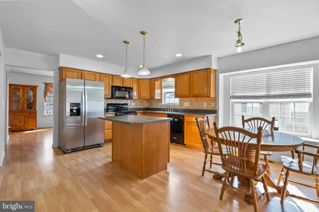 a kitchen with stainless steel appliances granite countertop a stove top oven a refrigerator a dining table and chairs with wooden floor