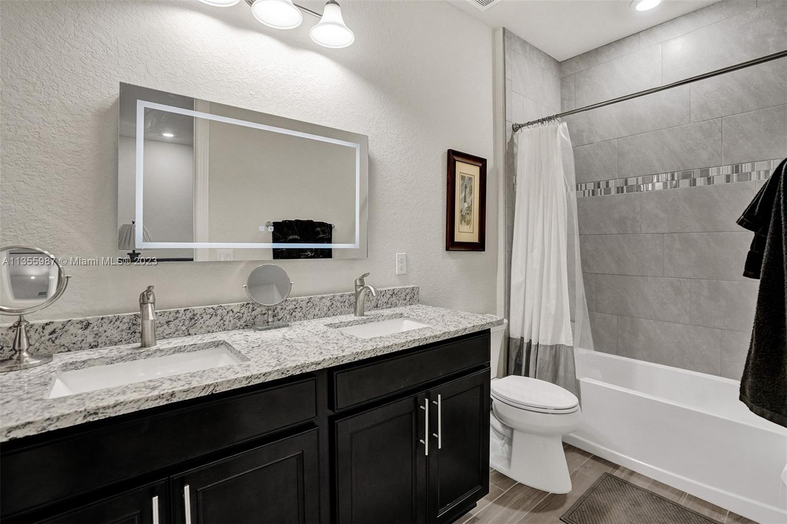 5055 Eucalyptus Drive Hollywood, FL 33021 - Photo 35 of 50 a bathroom with a granite countertop sink toilet a mirror a bathtub and shower