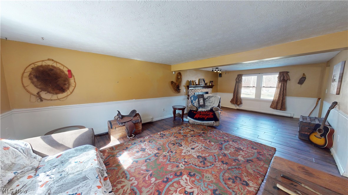 6970 Bushnell Road Conneaut, OH 44030 - Photo 12 of 28 Living room featuring a baseboard radiator, a fireplace, a textured ceiling, and dark wood-type flooring