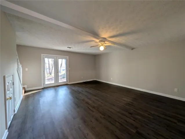 a view of an empty room with wooden floor and fan