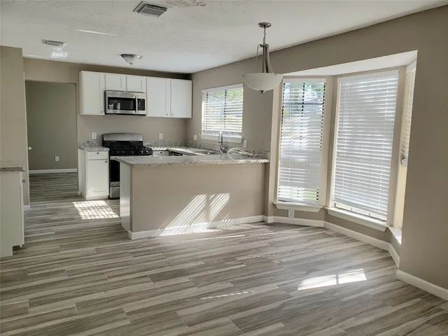 a kitchen with stainless steel appliances granite countertop a stove top oven a sink dishwasher a refrigerator and white cabinets with wooden floor