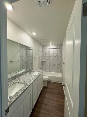 a bathroom with a granite countertop sink a toilet a mirror and bathtub