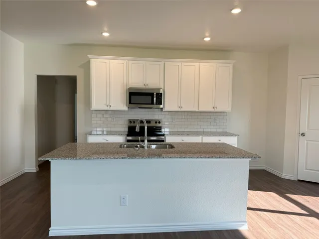 a kitchen with kitchen island granite countertop a sink a stove a refrigerator a microwave and cabinets