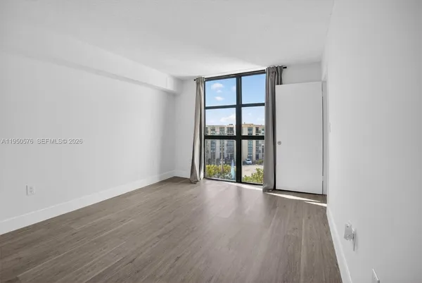 a view of an empty room with wooden floor and a window