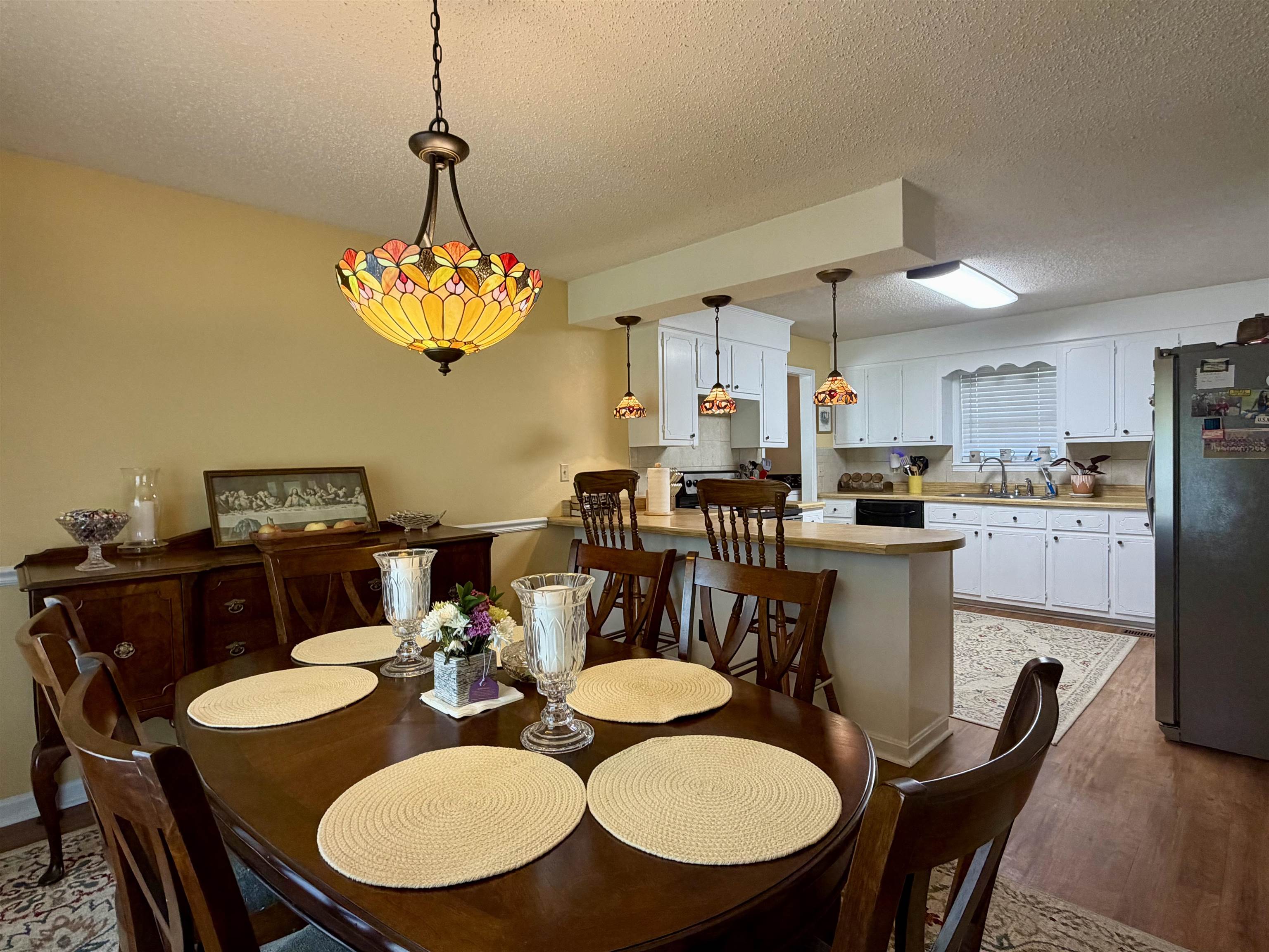 142 Treece Street Selmer, TN 38375 - Photo 11 of 36 Dining area featuring a decorative stained-glass style chandelier over a dark wood-finish dining table, with a kitchen visible in the background